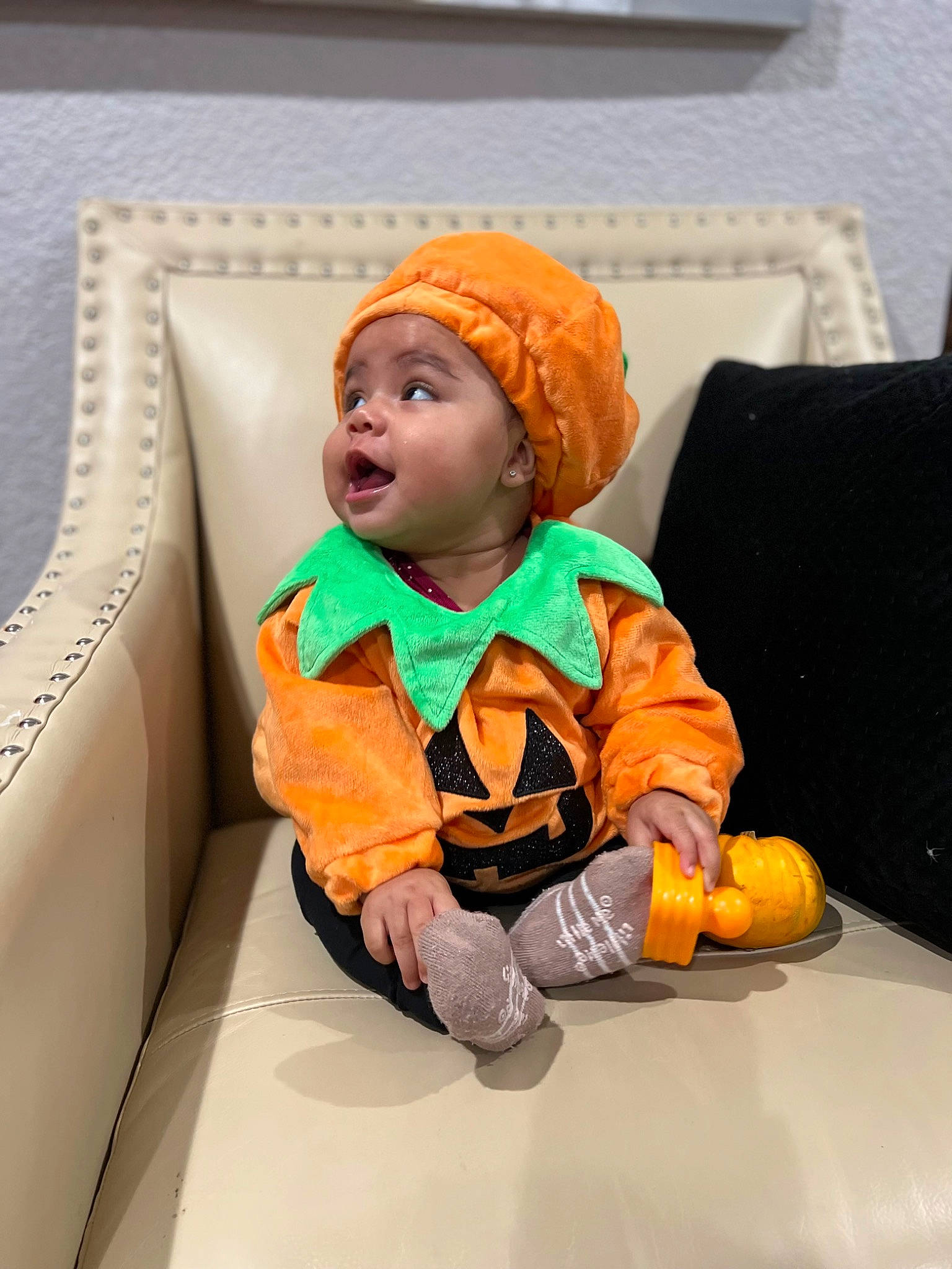 Alicia is registered to the contest to win money with this photo: baby, baby_toddler_clothing, child, comfort, flooring, headwear, jacket, orange, person, personal_protective_equipment, room, sitting, sleeve, throw_pillow, toddler