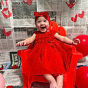 Ila Rose is registered to the contest to win money with this photo: baby, child, red_dress, headband, bow, red_chair, balloons, rose_petals, newspaper_backdrop, handprints, happy, smiling, sitting, indoor, cute, playful, portrait, decor, celebration, colorful