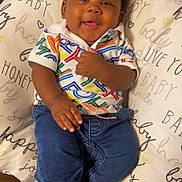 Jakai is registered to the contest to win money with this photo: baby, infant, smiling, child, clothing, jeans, colorful_shirt, pillow, cushion, text, happy, cute, indoors, person, skin, face, foot, hand, sitting, portrait