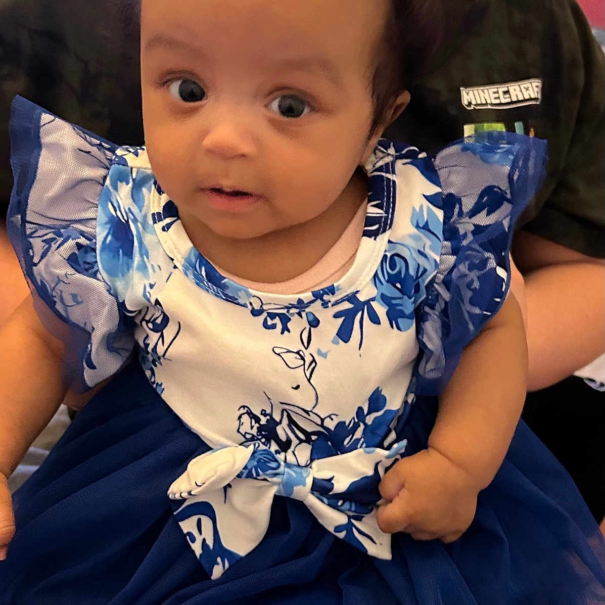 Chioma is registered to the contest to win money with this photo: baby, background, blue, bow, child, clothing, cute, dress, fabric, face, hand, holding, indoor, infant, minecraft, person, sitting, smile, white, young_child