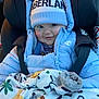 baby, child, car_seat, winter_clothing, puffer_jacket, beanie, blanket, animal_print, smile, face, cute, blue, warm, infant, cozy, sitting, person, clothing, headwear, indoors