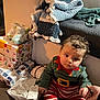 baby, child, christmas, pajamas, present, gift, wrapped_gift, blanket, couch, floor, hand, holding_hand, baby_shoes, knitted_blanket, striped_pants, indoor, holiday, cute, festive, person