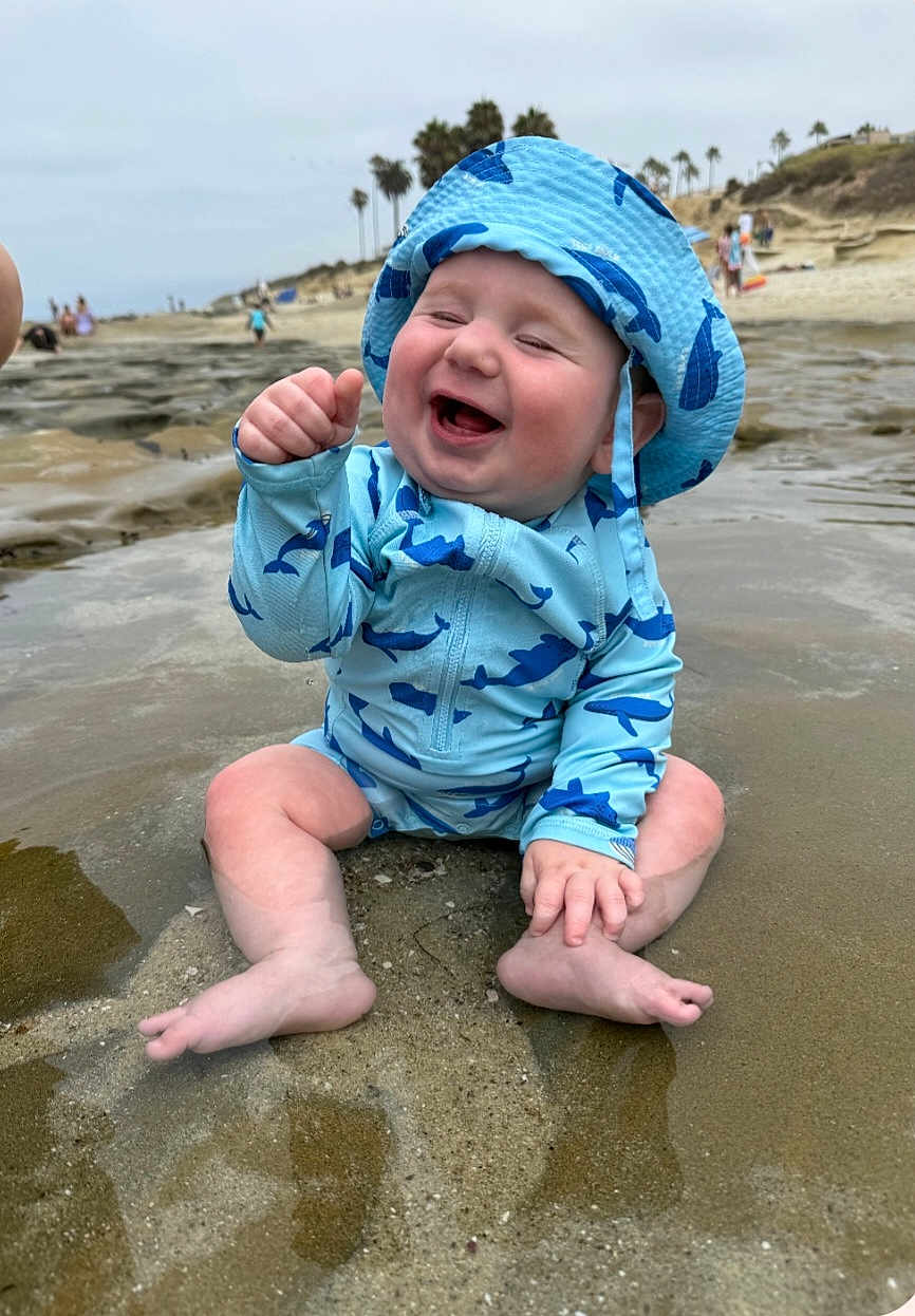 Jackson joined the competition — help win amazing prizes! baby, child, smiling, beach, water, swimsuit, hat, sunhat, sandy, palm_trees, ocean, happy, sitting, toddler, playful, summer, outdoor, nature, fun, vacation