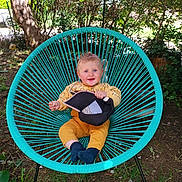Noé a rejoint le concours — aidez-le/la à gagner de superbes lots ! baby, child, smiling, blue_eyes, yellow_clothing, turquoise_chair, outdoor, greenery, grass, tree, cap, sitting, happy, nature, sunlight, portrait, young_child, cute, playful, garden