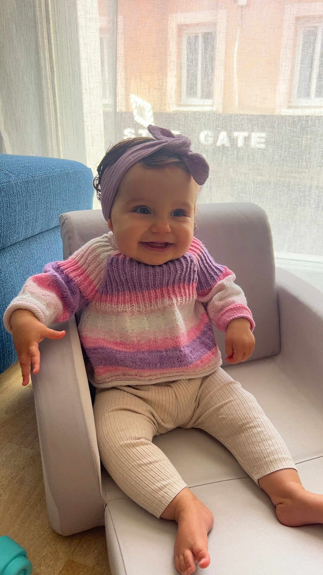 Aya a rejoint le concours — aidez-le/la à gagner de superbes lots ! baby, child, smiling, headband, purple, sweater, striped, pastel_colors, armchair, indoor, curtain, window, light, happy, seated, barefoot, person, cute, infant, cozy