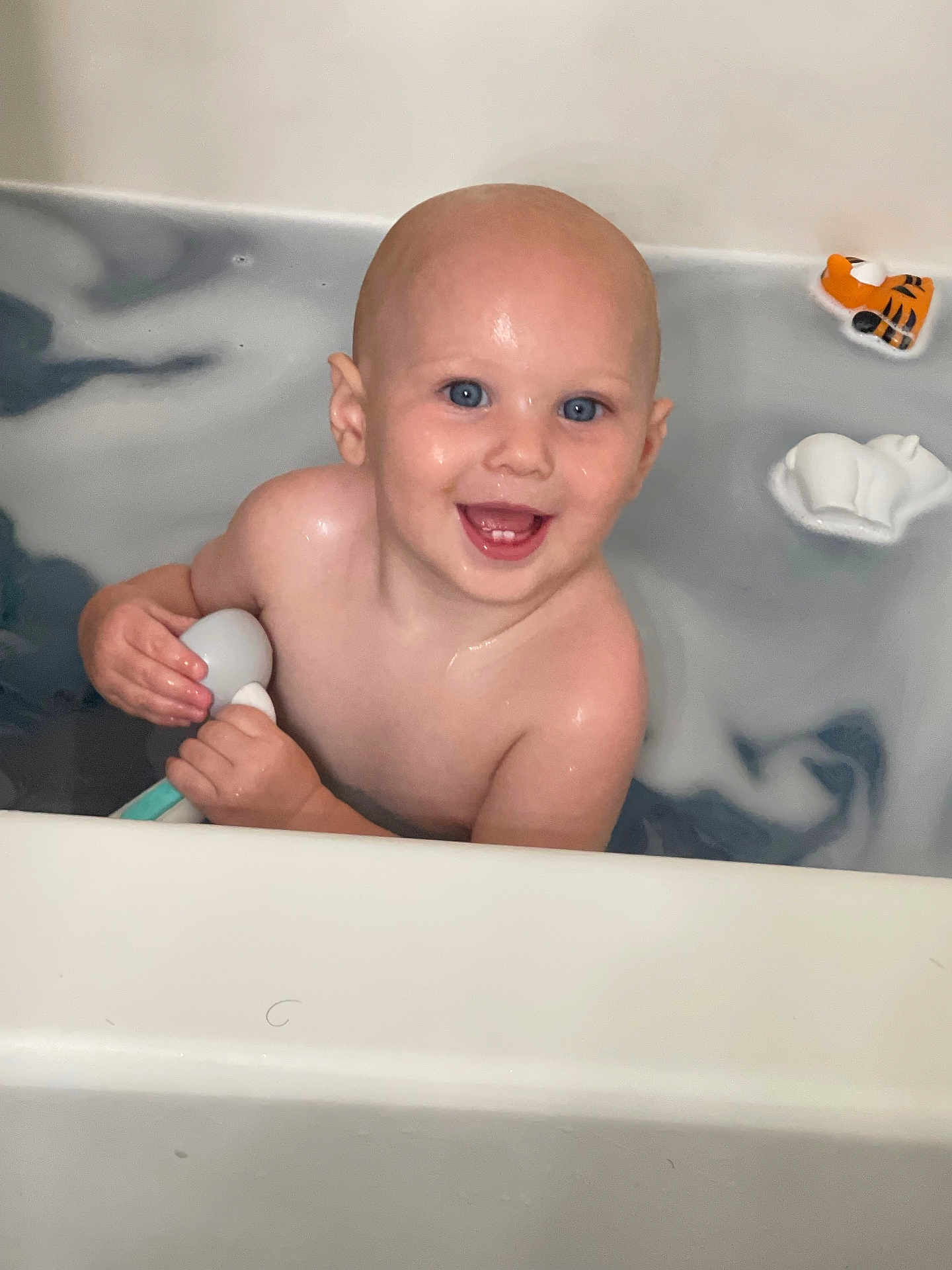 Dustin is registered to the contest to win money with this photo: baby, child, bathtub, bath, water, toy, smile, happy, blue_eyes, skin, head, bald, hand, sitting, wet, indoor, play, floating, person, cute