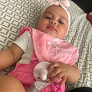 Aurélia is registered to the contest to win money with this photo: baby, infant, pacifier, headband, pink_bib, clothing, hand, bedspread, pattern, person, face, closeup, indoor, cute, child, resting, holding, baby_girl, soft_lighting, casual