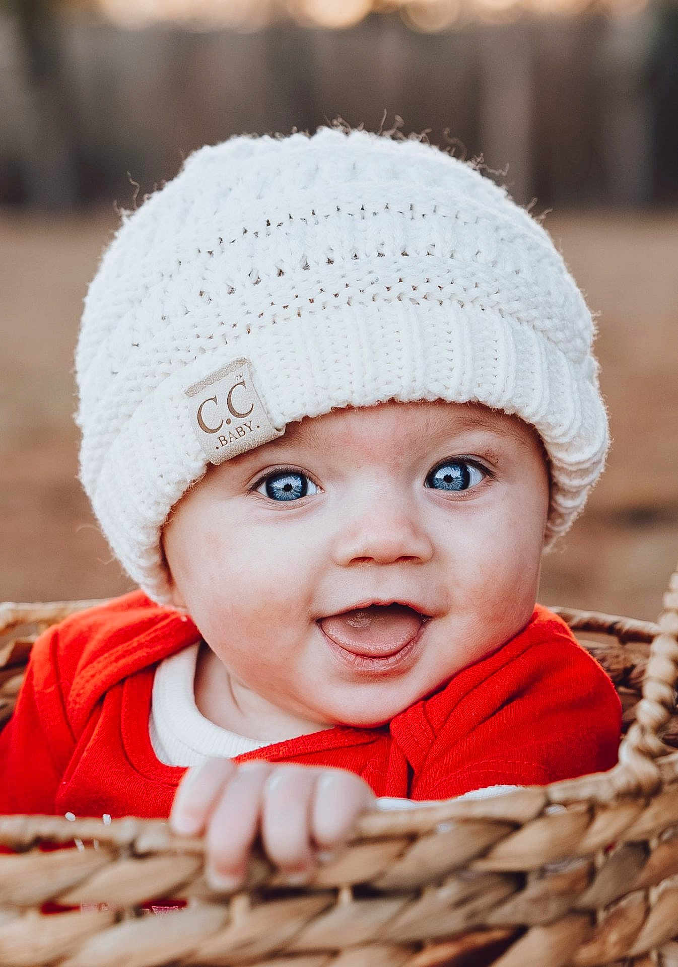 Opal is registered to the contest to win money with this photo: baby, child, infant, beanie, knit_hat, blue_eyes, smile, open_mouth, basket, wicker_basket, red_clothing, portrait, closeup, hand, outdoor, bokeh, cute, rosy_cheeks, clothing_tag, winter_hat
