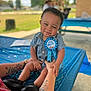 baby, child, smiling, birthday, ribbon, blue, table, tablecloth, outdoor, daylight, person, tattoo, hands, shoes, denim, cute, happy, celebration, park, blurred_background