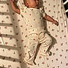 baby, infant, child, sleeping, lying_down, portrait, face, hands, arms, legs, onesie, strawberry_pattern, floral_bedding, mattress, crib, bedroom, indoor, warm_lighting, candid, baby_fashion