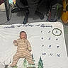 baby, infant, child, lying_down, milestone_blanket, three_months, striped_onesie, portrait, face, indoors, nursery, computer_desk, office_chair, carpet, blanket, woodland_theme, trees, bear, deer, wreath