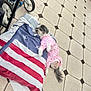dog, pajamas, pink, floor, tile, pillow, american_flag, towel, paw, tail, stroller_wheel, foot, indoor, pet, relaxed, lying_down, pattern, small_dog, home, casual