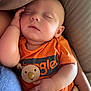 baby, sleeping, orange_shirt, pacifier, blanket, arm, hand, face, infant, cozy, resting, child, cute, comfort, toddler, closeup, indoor, soft_lighting, peaceful, portrait