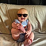 Waylon is registered to the contest to win money with this photo: baby, sunglasses, smile, couch, blue_striped_clothing, foot, hand, infant, happy, indoors, cute, person, head, skin, sitting, plush, relaxed, comfort, expression, portrait