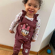 Lilya participe au concours pour gagner de l'argent avec cette photo : toddler, child, smiling, curly_hair, indoor, overalls, daisy_duck, boots, wooden_floor, wall, standing, happy, clothing, person, footwear, cute, young_child, playful, portrait, fashion