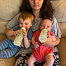 baby, blue_clothing, bottle, casual_clothing, child, couch, family, feeding, happy, holding, home, indoor, infant, parent, person, red_clothing, relaxing, sitting, striped_clothing, woman