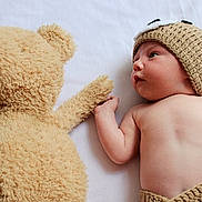 Mark is registered to the contest to win money with this photo: baby, infant, teddy_bear, knitted_hat, knitted_shorts, cute, soft_toy, white_sheet, holding_hands, lying_down, child, plush_toy, portrait, adorable, face, skin, cuteness, hat, toy, baby_boy