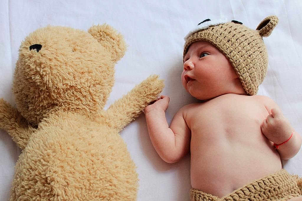 Mark is registered to the contest to win money with this photo: baby, infant, teddy_bear, knitted_hat, knitted_shorts, cute, soft_toy, white_sheet, holding_hands, lying_down, child, plush_toy, portrait, adorable, face, skin, cuteness, hat, toy, baby_boy