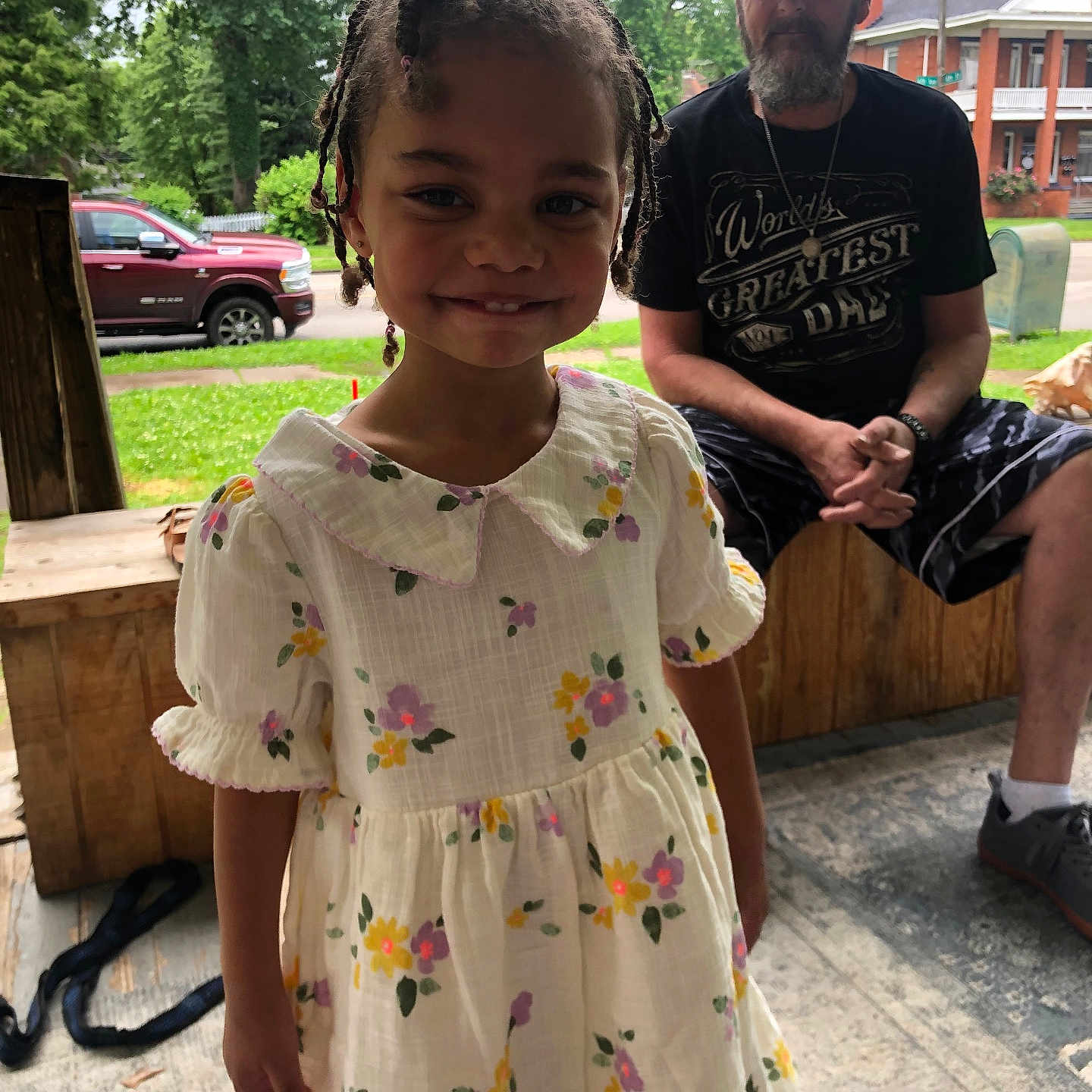 Bailey is registered to the contest to win money with this photo: beard, bench, braids, cap, casual_clothing, child, daytime, dress, floral_pattern, girl, greenery, happy, house, man, outdoor, portrait, sidewalk, smile, trees, truck