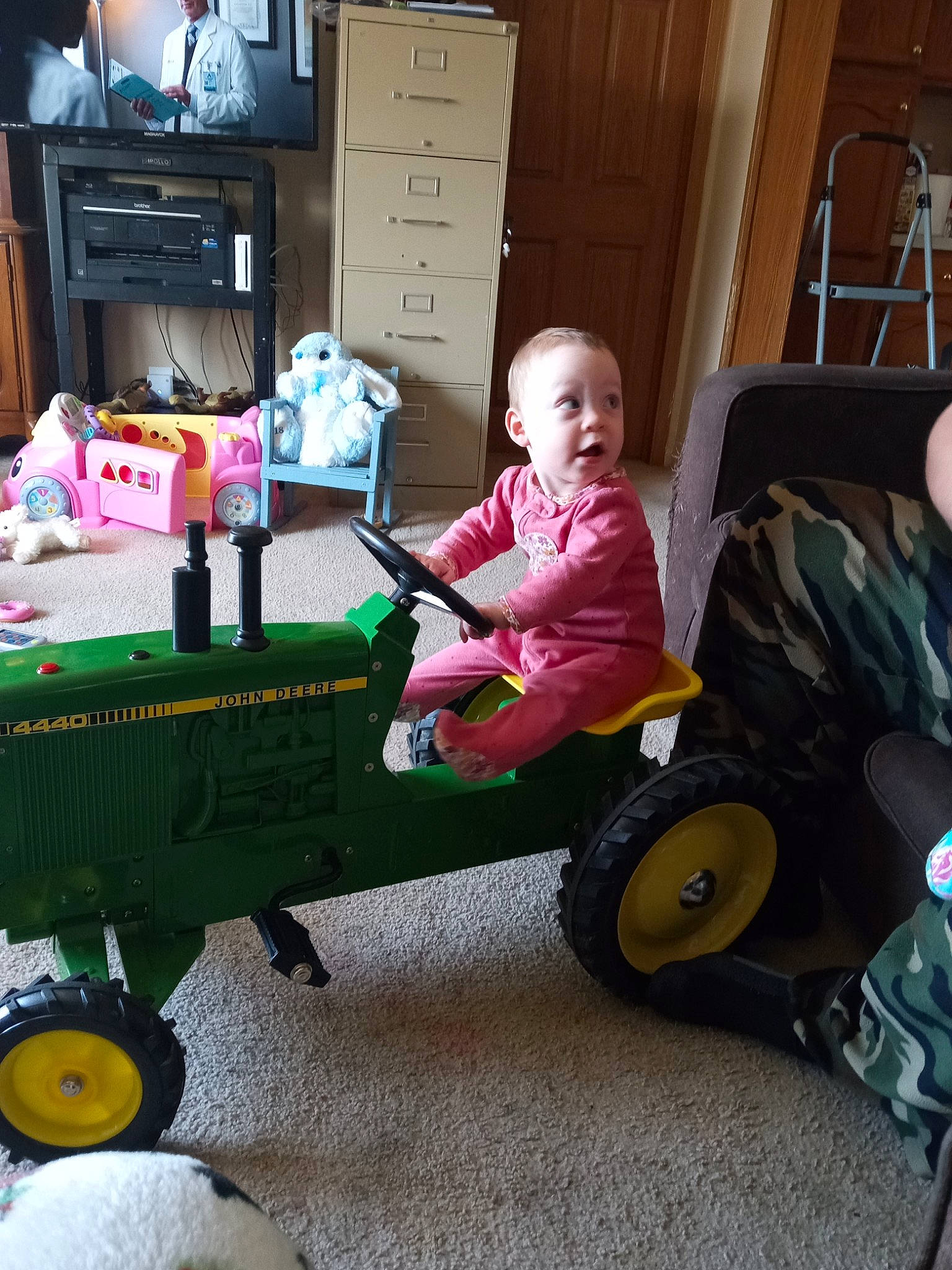 Baylee is registered to the contest to win money with this photo: baby, baby_products, baby_toddler_clothing, cabinetry, chest_of_drawers, child, comfort, drawer, flooring, fun, home_appliance, person, play, sitting, surprise, television, tire, toddler, toy, tractor