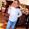 child, girl, portrait, smiling, peace_sign, braided_hair, beads, sweater, jeans, yellow_boots, standing, indoor, living_room, couch, armchair, rug, fireplace, home_decor, school, text_overlay