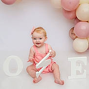 Grace joined the competition — help win amazing prizes! baby, child, pink_clothing, headband, balloons, birthday, number_one, white_floor, smiling, sitting, celebration, decorations, pastel_colors, cute, portrait, indoor, happy, one_year_old, festive, infant