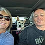 Sandy is registered to the contest to win money with this photo: woman, man, dog, car_interior, seatbelt, sunglasses, smile, casual_clothing, pet, road_trip, happy, seat, headrest, collar, window, daylight, backseat, harness, portrait, people