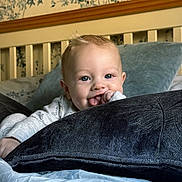 George joined the competition — help win amazing prizes! baby, child, bed, pillow, blue_eyes, blanket, indoor, smiling, cute, portrait, home, headboard, wallpaper, cozy, infant, person, hand, clothing, face, toddler