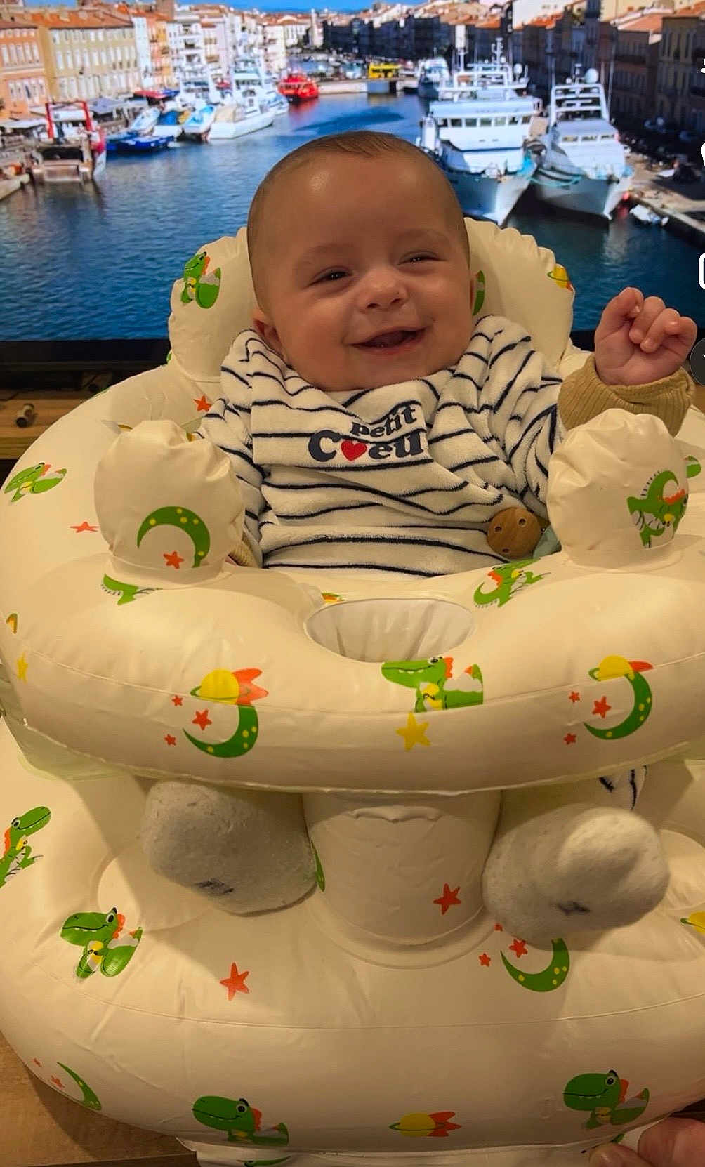 Eden participe au concours pour gagner de l'argent avec cette photo : baby, infant, smiling, inflatable_seat, baby_seat, striped_clothing, bib, socks, wooden_toy, tv_background, boats, harbor, water, indoor, happy, closeup, dinosaur_pattern, stars, moons, television