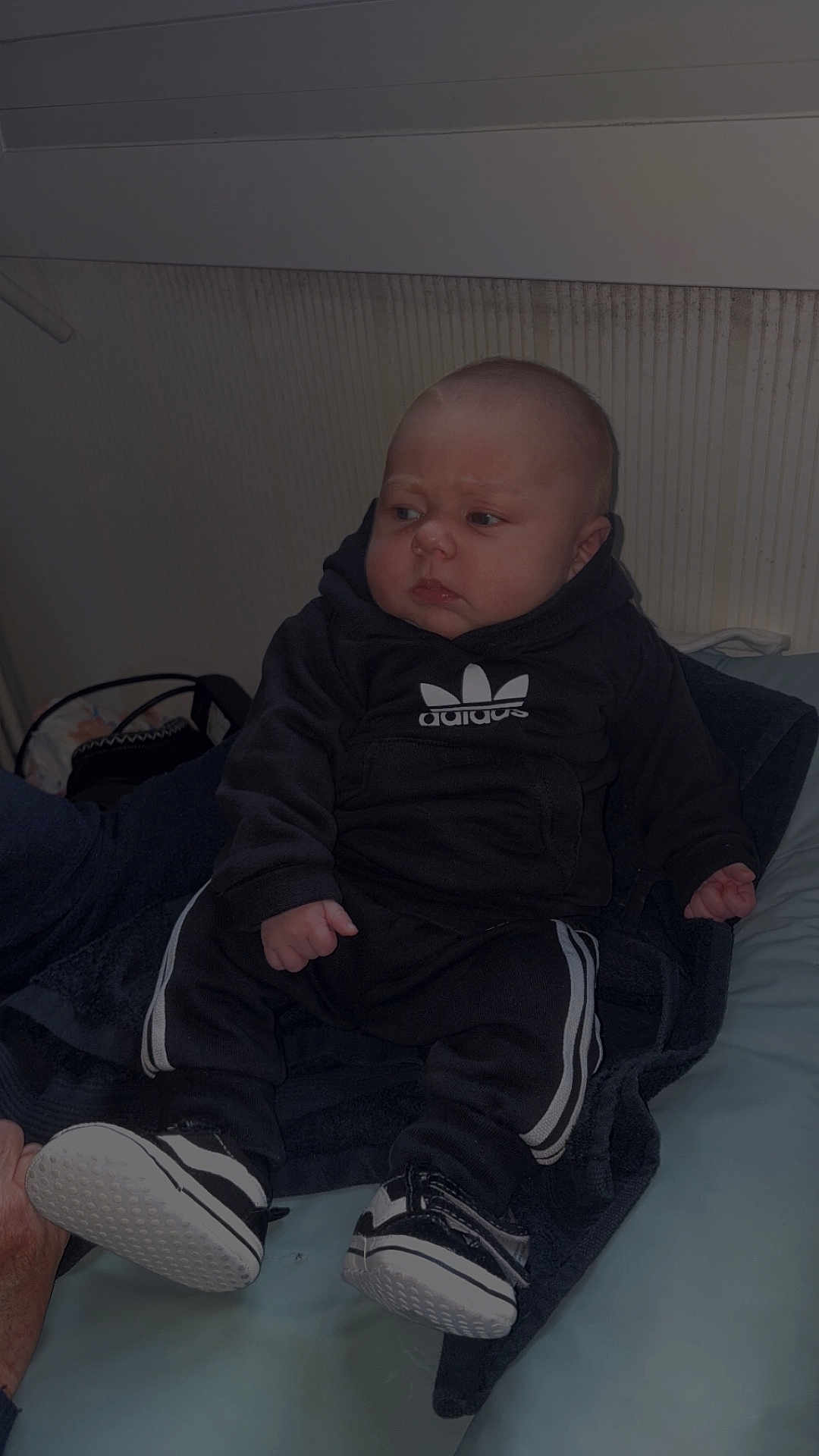 Tommy a rejoint le concours — aidez-le/la à gagner de superbes lots ! baby, child, infant, black_clothing, hoodie, sneakers, indoor, sitting, person, footwear, tracksuit, young_child, apparel, casual_wear, cute, portrait, expression, resting, soft_surface, hand