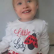 Valerie is registered to the contest to win money with this photo: toddler, child, smiling, face, clothing, ladybug, red_bow, white_shirt, patterned_skirt, indoor, portrait, happy, cute, sitting, young_child, wall, decor, hearts, fashion, kid