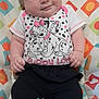 Alaina joined the competition — help win amazing prizes! baby, infant, smiling, closed_eyes, cute, child, sitting, clothing, puppy_love, graphic_tee, patterned_background, colorful, black_pants, chubby_cheeks, happy, portrait, indoors, young_child, peaceful, seated