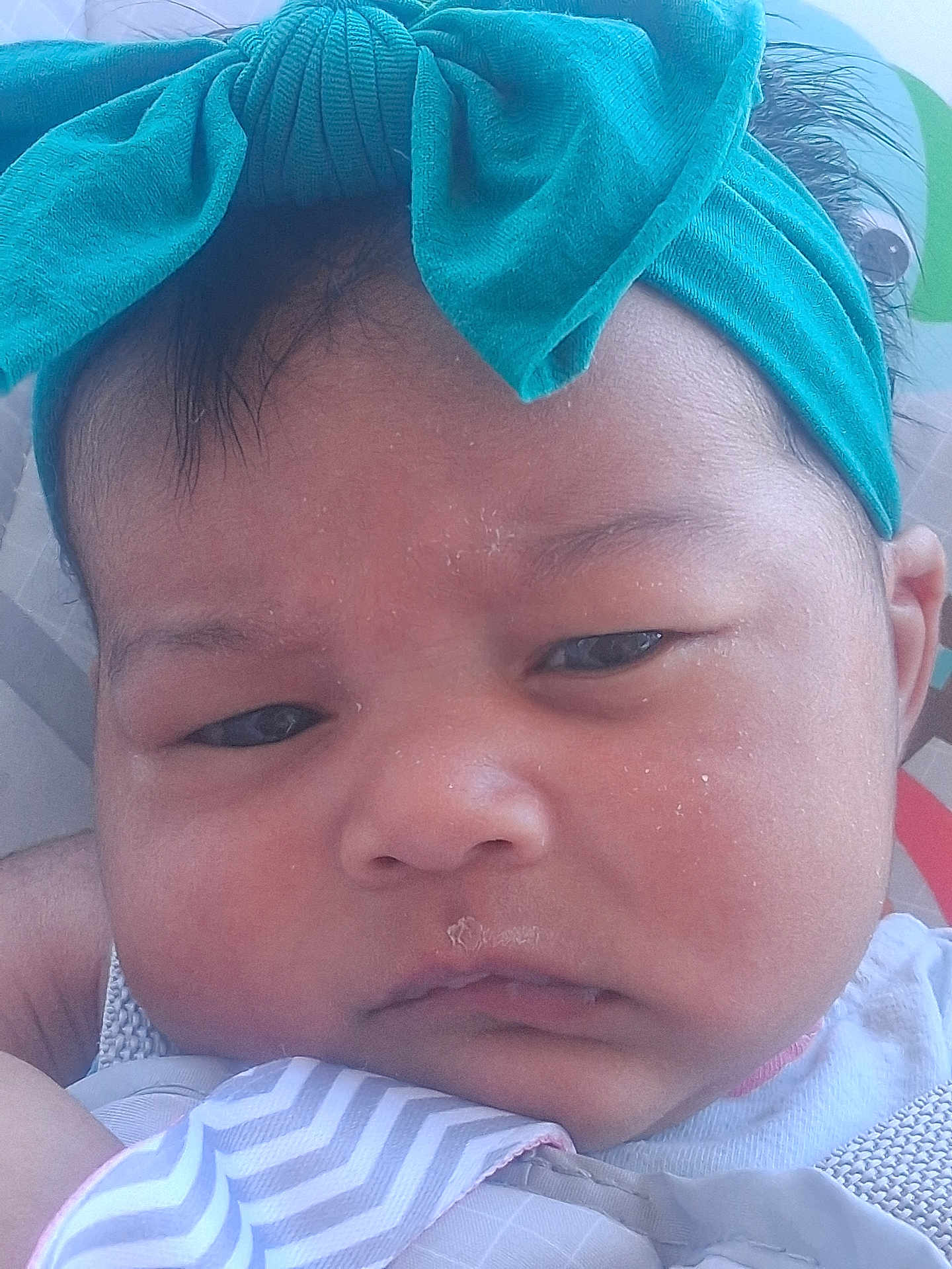 Nadaijah is registered to the contest to win money with this photo: baby, close_up, headband, bow, infant, face, skin, expression, serious, blanket, pattern, child, newborn, portrait, cute, wearing, apparel, indoors, young, person