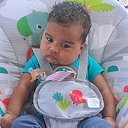 Nadaijah joined the competition — help win amazing prizes! baby, child, infant, curly_hair, pacifier, baby_seat, colorful, animal_print, toy, clothing, blue_shirt, pants, straps, indoors, seat, cute, expression, face, person, sitting