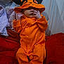 Kyra-Violet is registered to the contest to win money with this photo: baby, infant, orange_onesie, hood, black_ears, blanket, red_blanket, purple_blanket, lying_down, indoor, cute, small_hands, face, cozy, child, person, sleepwear, soft_fabric, resting, newborn