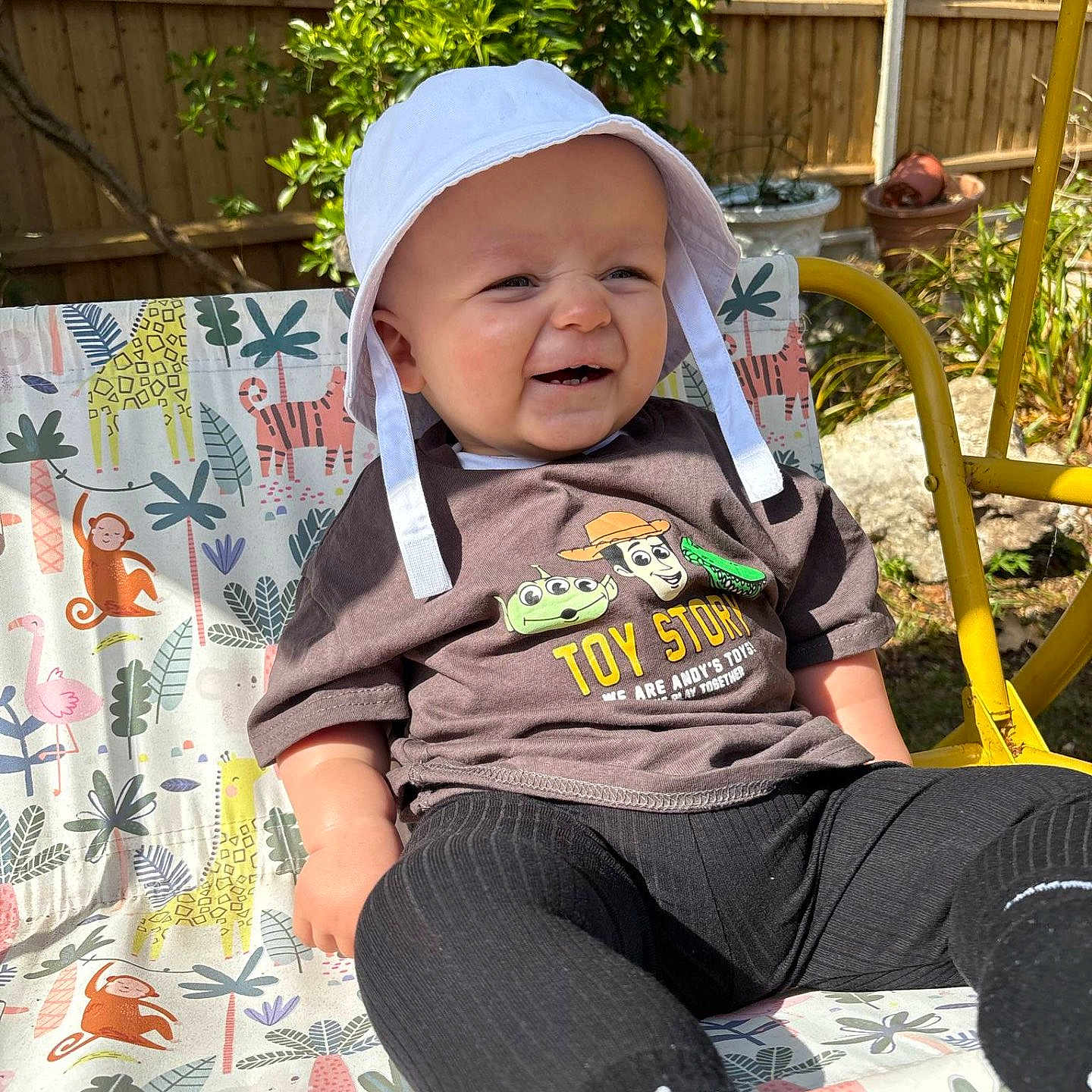Cohen-Jay is registered to the contest to win money with this photo: animal_print, baby, black_leggings, chair, child, daylight, fence, garden, happy, hat, legs, outdoor, patterned_chair, plants, playful, smiling, sunny, toy_story, tshirt, white_hat