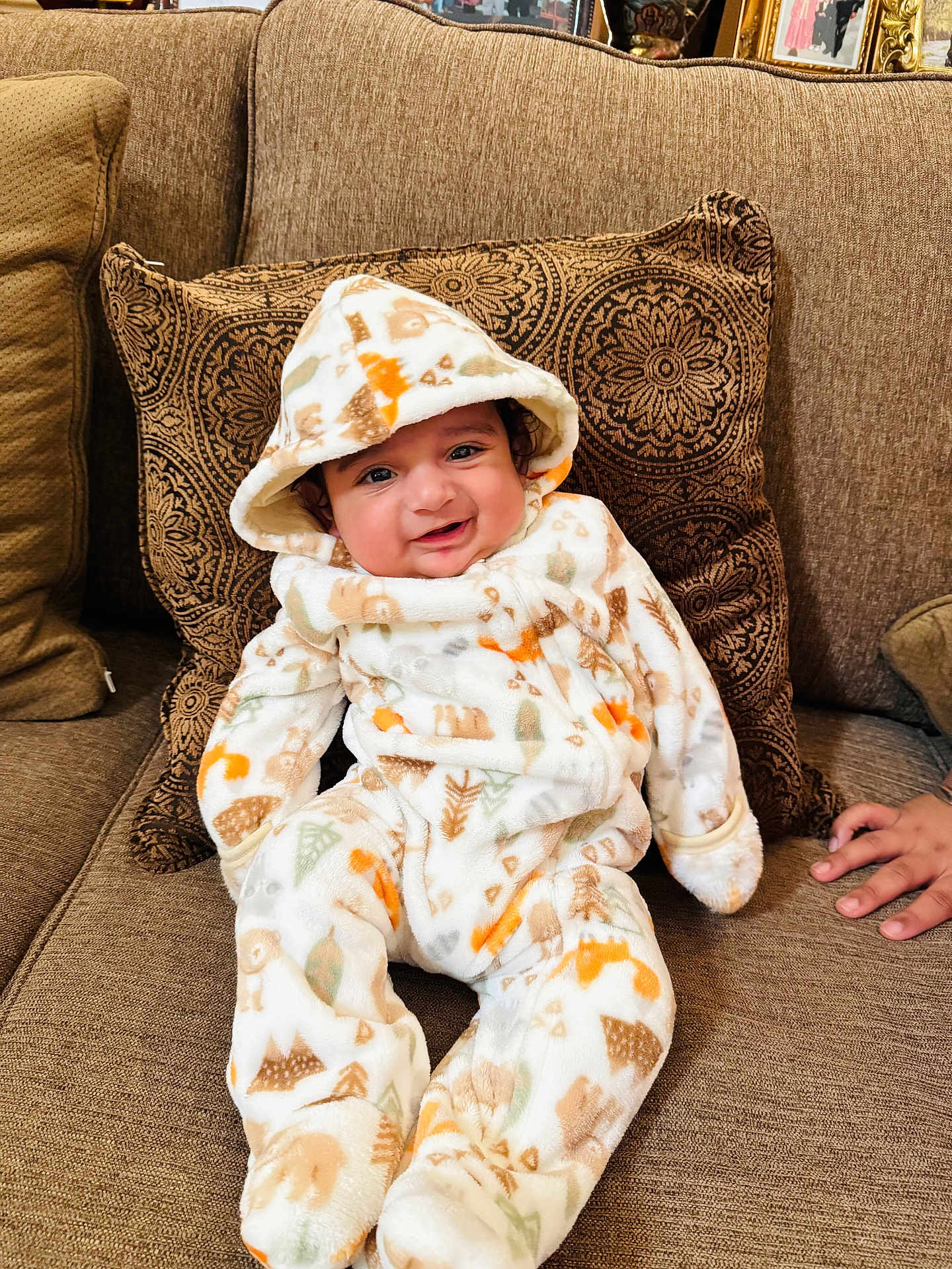 Gurarnaaz joined the competition — help win amazing prizes! baby, infant, smile, hooded_onesie, couch, pillow, brown, patterned_clothing, indoor, child, cozy, happy, portrait, person, hand, furniture, home, cute, sitting, face