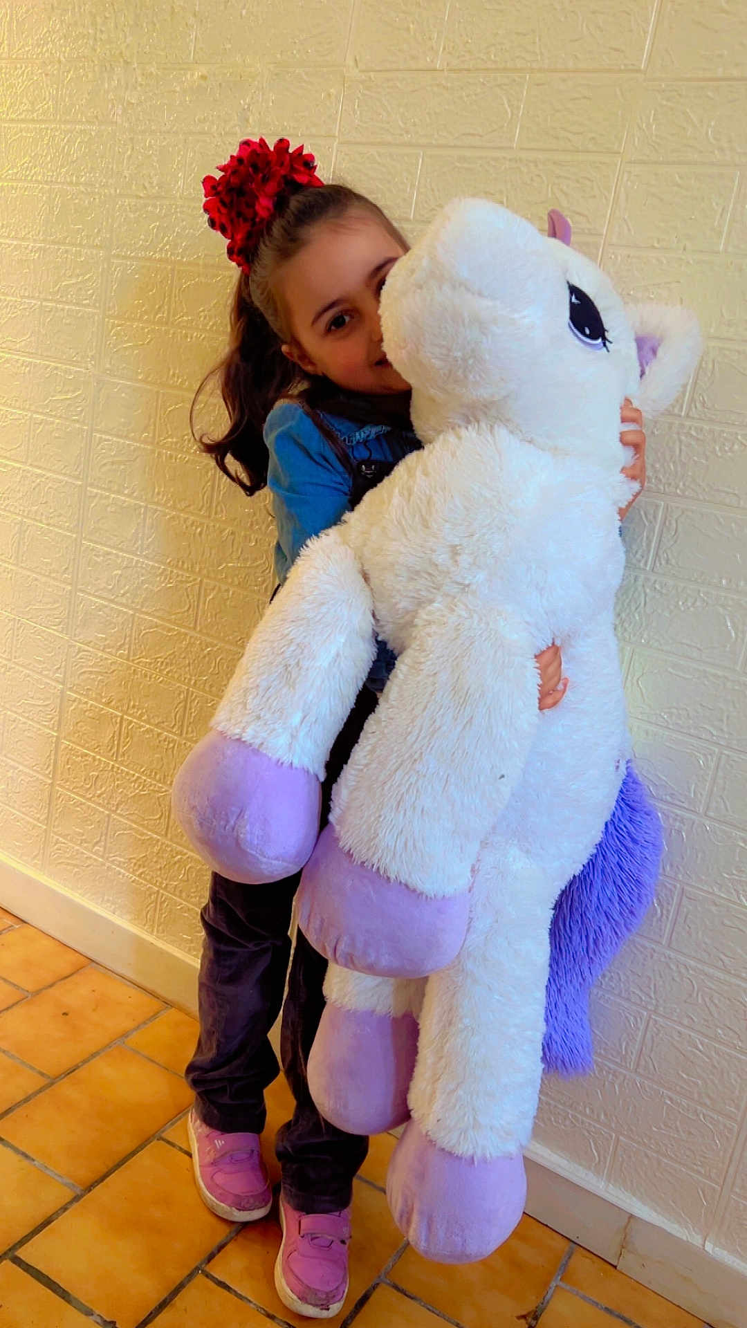 Kenza a rejoint le concours — aidez-le/la à gagner de superbes lots ! child, girl, plush_toy, unicorn, stuffed_animal, indoor, wall, tile_floor, happy, smiling, casual_clothing, hair_accessory, purple, pink_shoes, toy, cute, childhood, playful, soft_toy, home