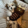 dog, puppy, plush_toy, owl_toy, cushion, soft_fabric, wood_floor, pet, cute, fluffy, snuggling, indoor, cozy, resting, small_dog, furry, toy, relaxing, home, sleepy
