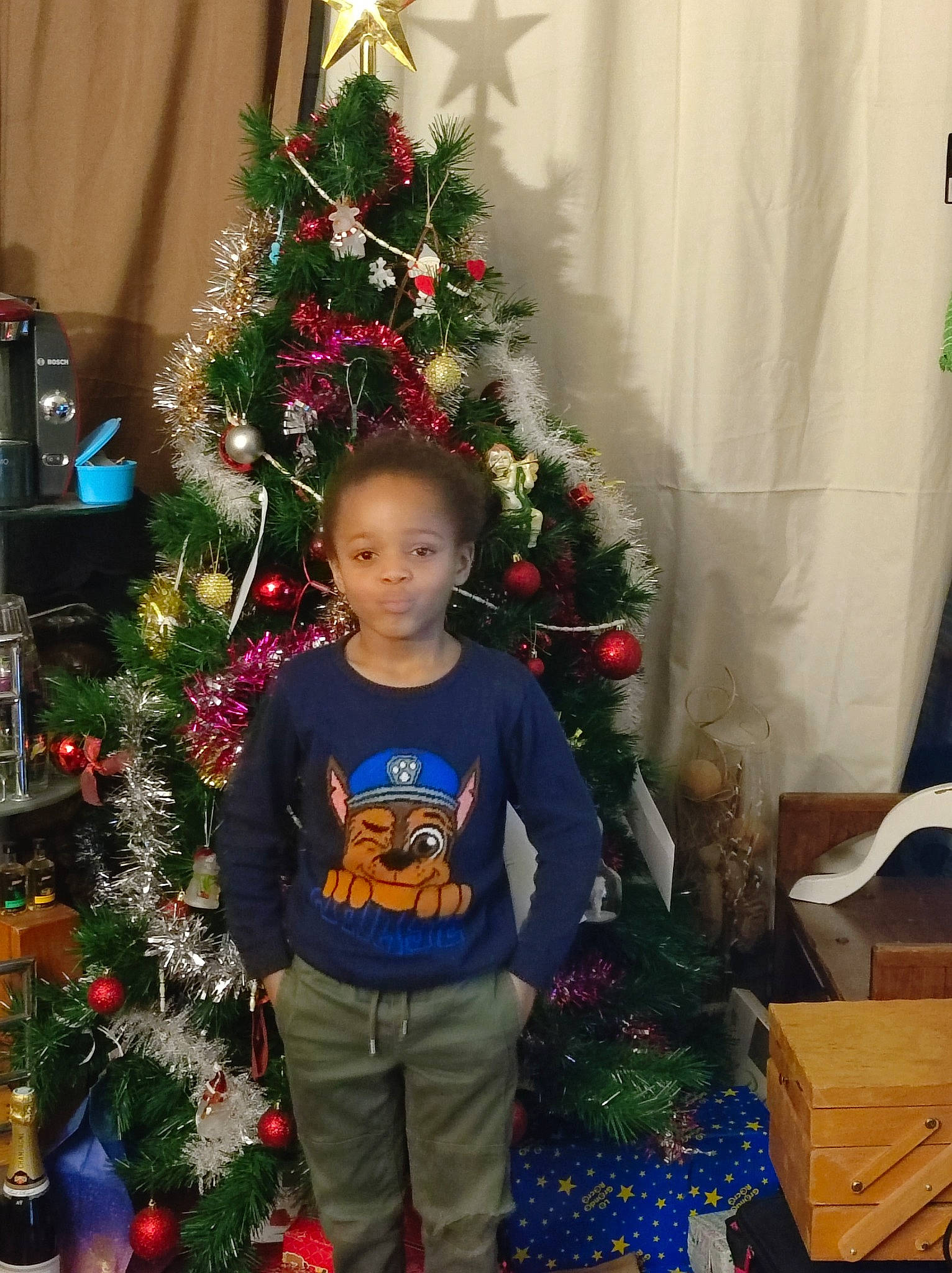 Kalvyn a rejoint le concours — aidez-le/la à gagner de superbes lots ! christmas, christmas_decoration, christmas_ornament, christmas_tree, conifer, curtain, event, evergreen, fun, happy, holiday, holiday_ornament, ornament, person, plant, room, shipping_box, standing, toddler, tradition