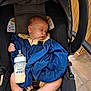 baby, sleeping, car_seat, blanket, milk_bottle, infant, child, foot, hand, clothing, indoor, wooden_wall, floor, seat_belt, face, peaceful, relaxation, cute, newborn, rest