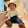 baby, child, cowboy_hat, hat, jeans, white_shirt, brown_shoes, armchair, furniture, indoor, smiling, face, person, cute, seated, floor_lamp, curtains, home, casual, portrait