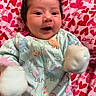 Delilah is registered to the contest to win money with this photo: baby, infant, child, smiling, happy, portrait, lying_down, onesie, dinosaur_pattern, mittens, white_mittens, blanket, heart_pattern, pink, red, indoor, close_up, face, baby_clothing, adorable