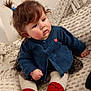 baby, child, blue_cardigan, red_booties, tights, blanket, knitted, pony_tail, curly_hair, indoor, cute, sitting, cozy, texture, soft, clothing, face, portrait, young_child, pink_cheeks