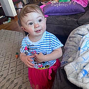 Mckenna is registered to the contest to win money with this photo: toddler, child, indoor, carpet, couch, pillow, blanket, clothing, minnie_mouse, tutu, striped_shirt, smiling, curious, floor, furniture, home, person, young_child, earrings, playful