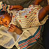 baby, infant, towel, striped_towel, strawberry_pattern, romper, clothing, lying_down, curly_hair, skin, hand, foot, socks, bed, comfortable, indoor, portrait, cute, child, person