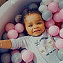child, toddler, smiling, ball_pit, pastel_colors, curly_hair, onesie, indoor, happy, playful, pink_balls, gray_balls, white_balls, cute, portrait, baby, leisure, cozy, relaxed, fun