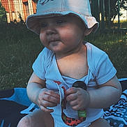 Jade participe au concours pour gagner de l'argent avec cette photo : baby, blanket, bucket_hat, child, clothing, cute, face, fence, grass, hands, hat, infant, legs, nature, outdoor, pacifier, person, sitting, sunlight, toy