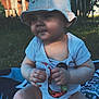 baby, blanket, bucket_hat, child, clothing, cute, face, fence, grass, hands, hat, infant, legs, nature, outdoor, pacifier, person, sitting, sunlight, toy