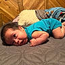baby, infant, child, lying_down, tummy_time, portrait, face, eyes, smiling, blue_shirt, short_hair, bare_feet, bed, blanket, pillow, bedspread, wooden_wall, indoor, cozy, photography